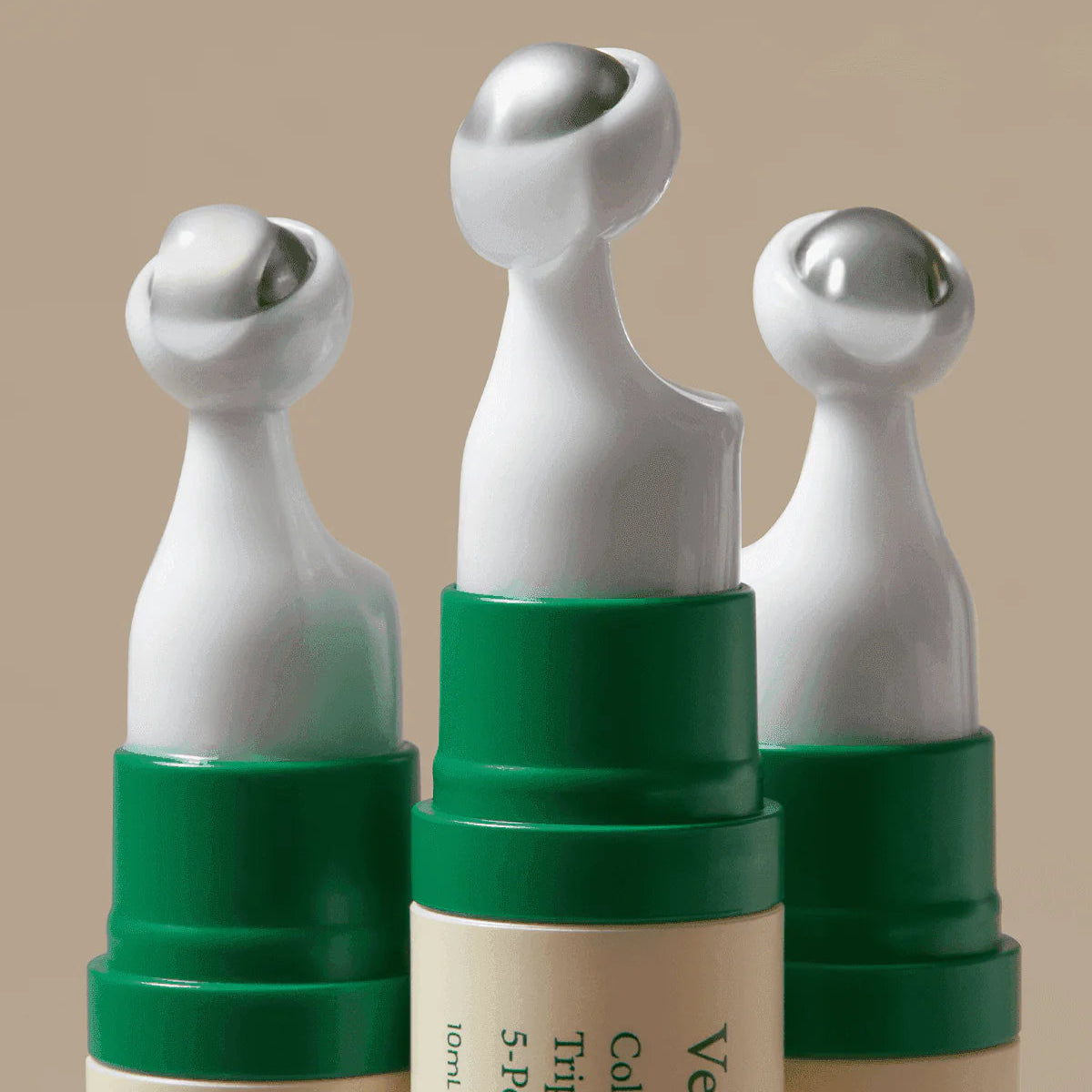 Three skincare devices with green caps on a beige background